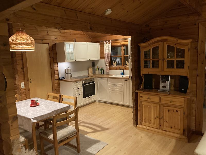Essbereich mit Holztisch und Stühlen, dahinter die helle Landhausküche