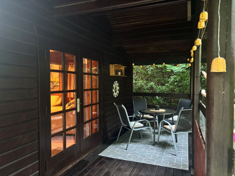 Überdachte Terrasse des Ferienhauses mit Sitzgruppe und Lichterkette, dahinter grüner Wald