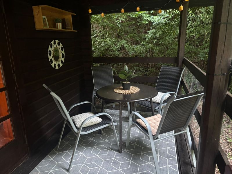 Sitzplatz auf der Terrasse mit vier Stühlen, Spiegel und Wandregal vor dem Wald